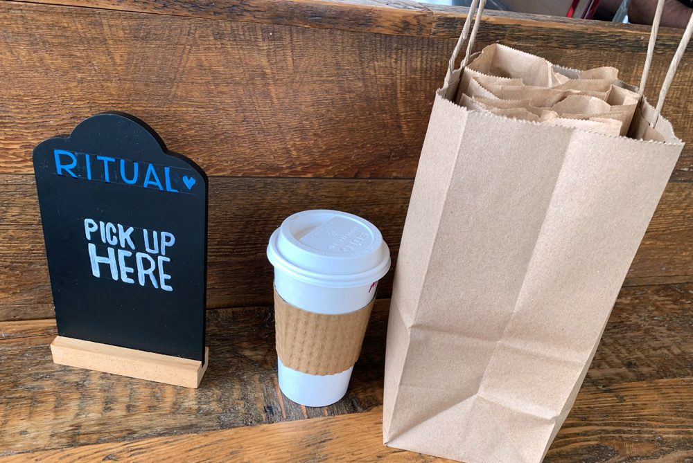 A cup of coffee and paper bag on the table.